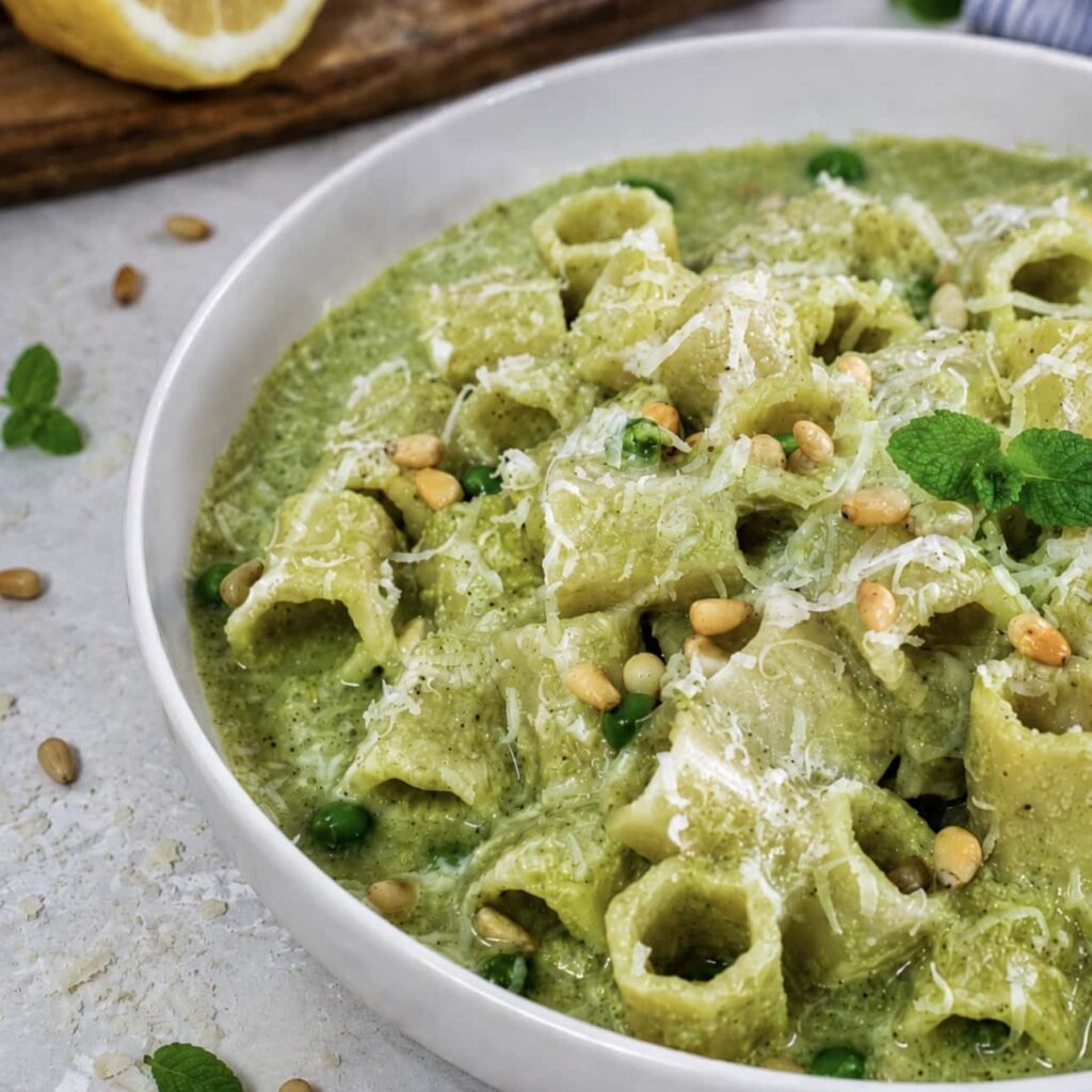 High-protein pea and mint pasta served on a plate with Parmesan, peas, toasted pine nuts and mint.
