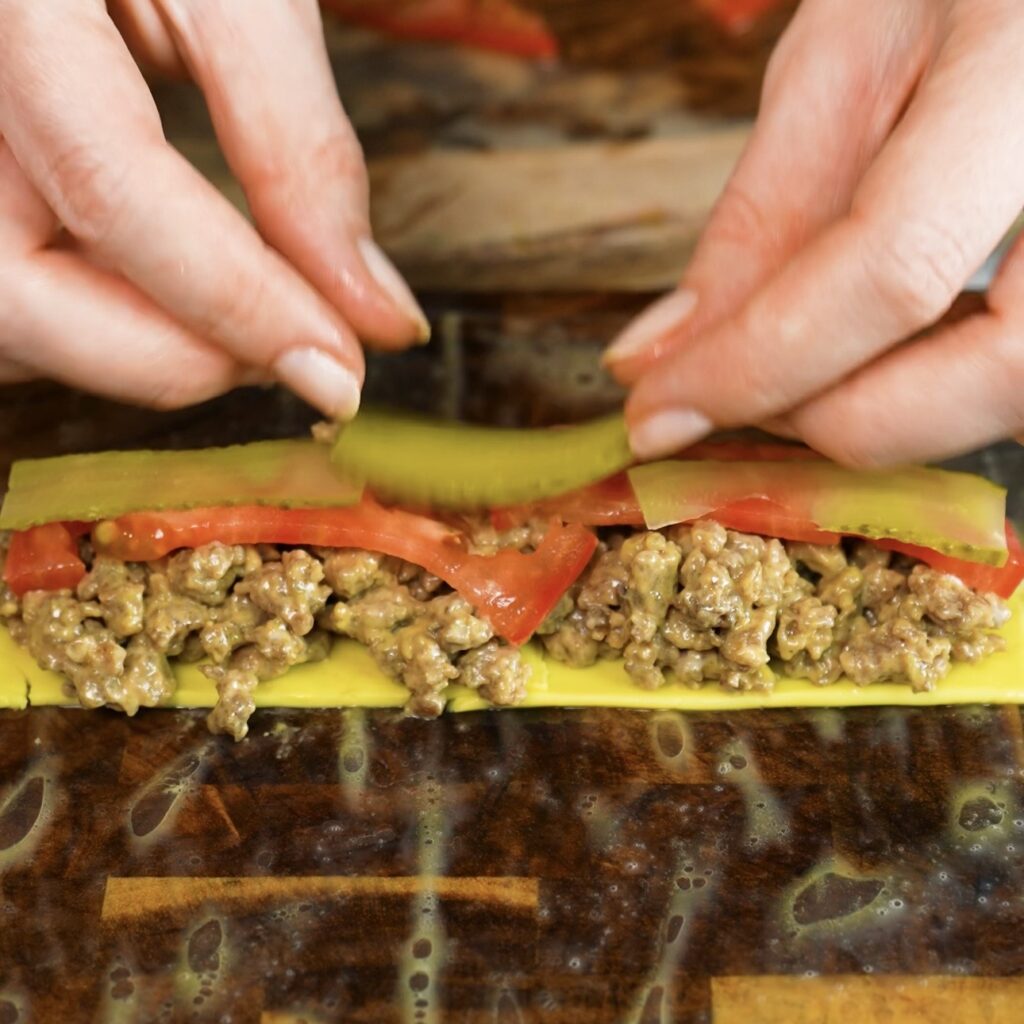 Adding cheeseburger filling to rice paper with beef, cheese, tomato and gherkins