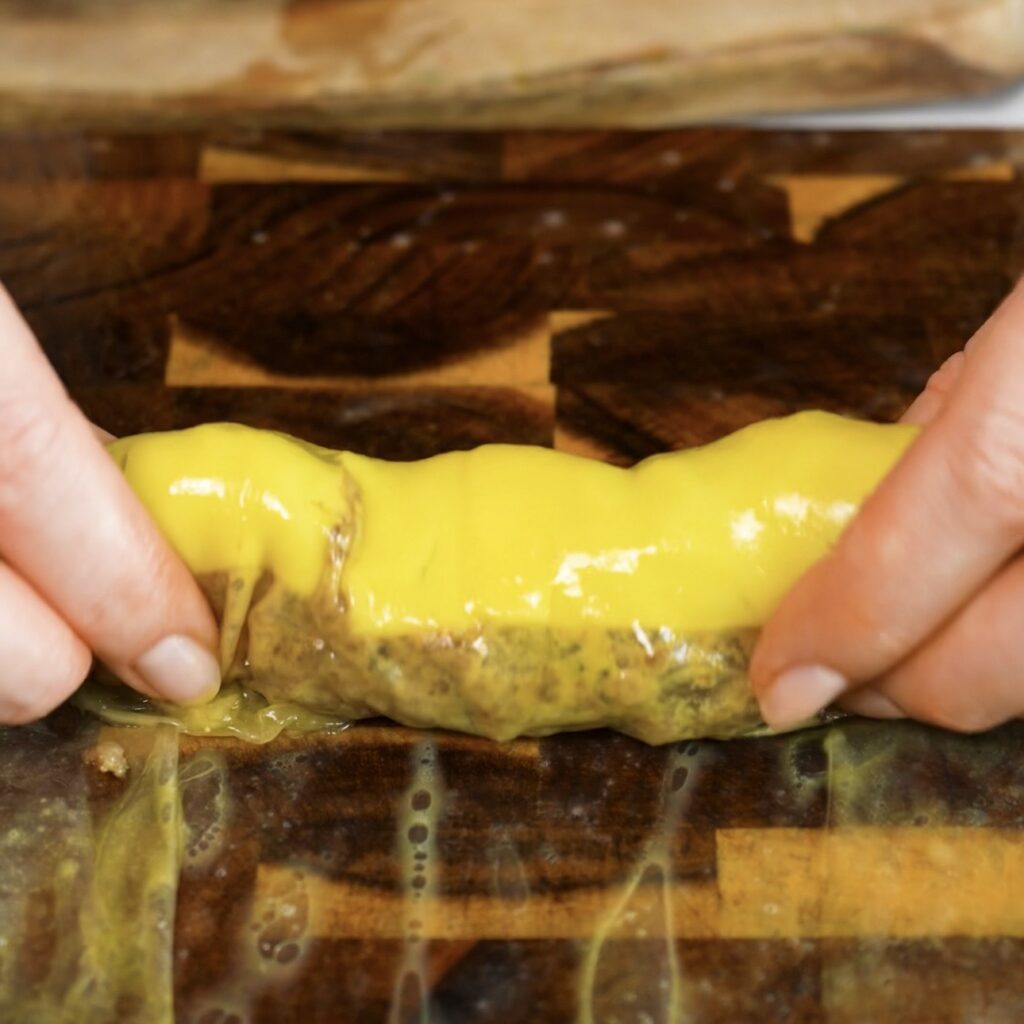 Rolling rice paper around cheeseburger filling with beef, cheese, tomato and gherkins