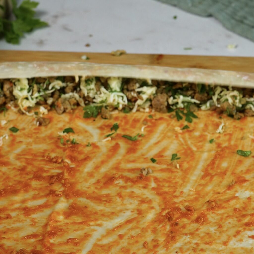 Rolling a filo sheet filled with minced beef, mozzarella and sun-dried tomato pesto.