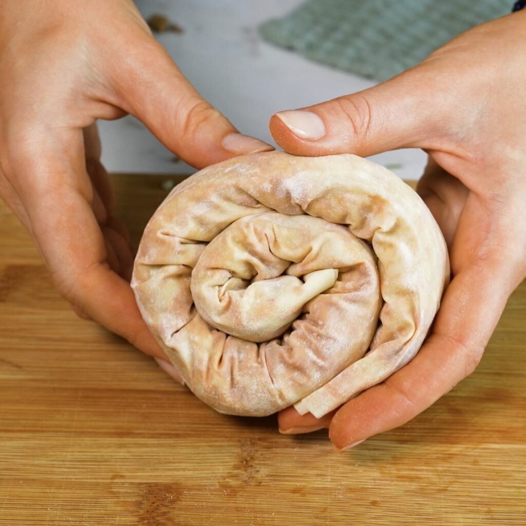 Hands holding a rolled filo swirl filled with cheesy beef filling.