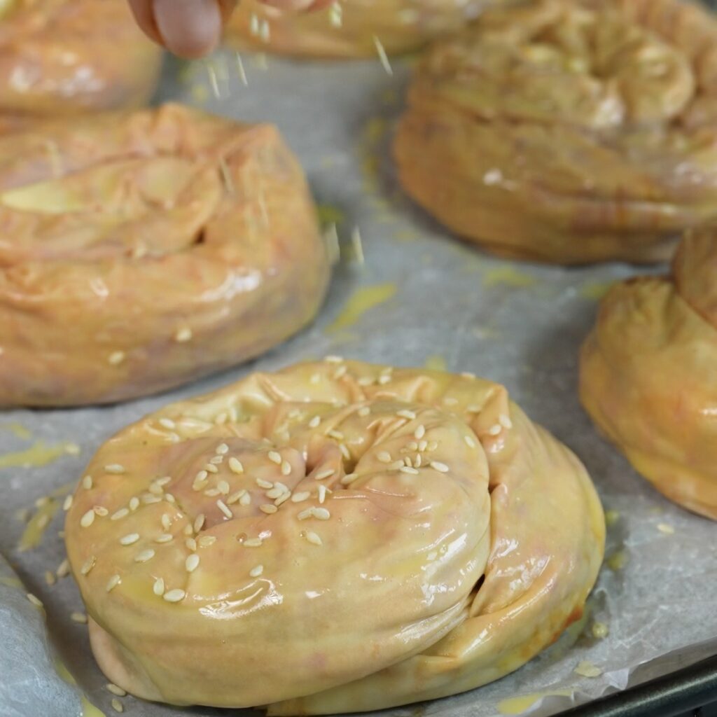 Cheesy beef filo swirls on a baking tray brushed with egg wash and sprinkled with sesame seeds.