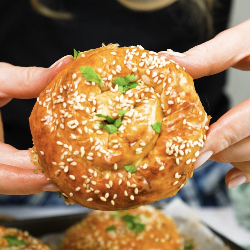 Hands holding a baked cheesy beef filo swirl.