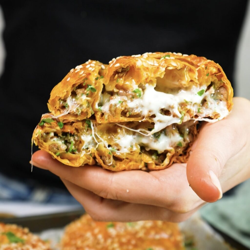 Hand holding a cheesy beef filo swirl cut in half.