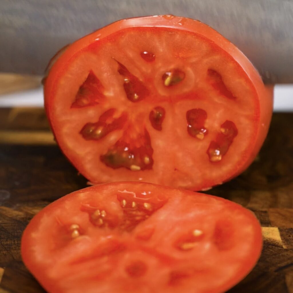 Slicing fresh tomatoes on a chopping board for a tomato and stracciatella upside-down tart.