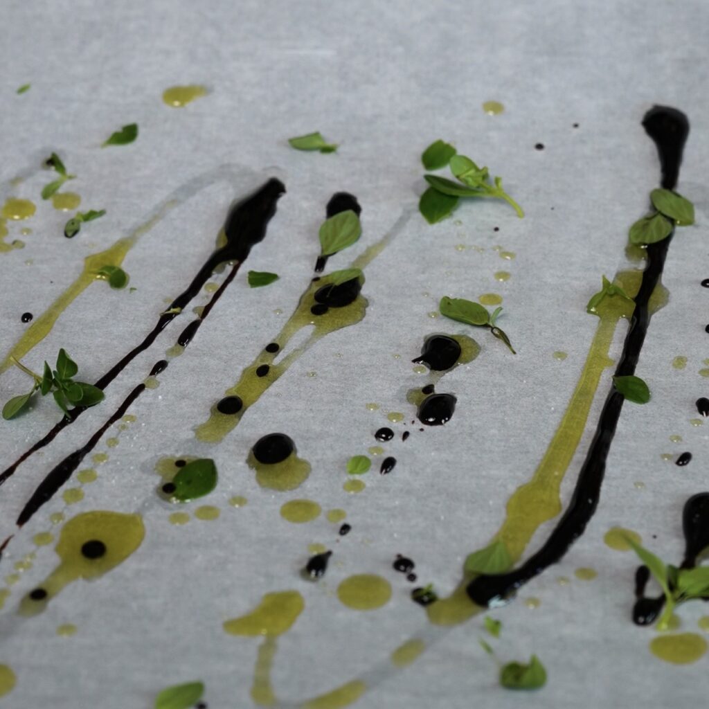 Olive oil, balsamic glaze, thyme leaves and salt arranged on parchment paper for a tomato and stracciatella upside-down tart.