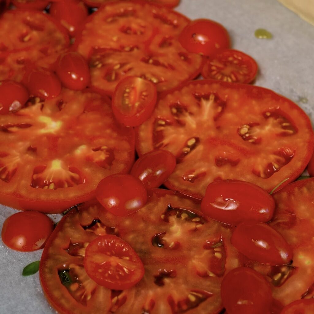 Sliced tomatoes arranged on parchment paper over olive oil, balsamic glaze, thyme and salt.