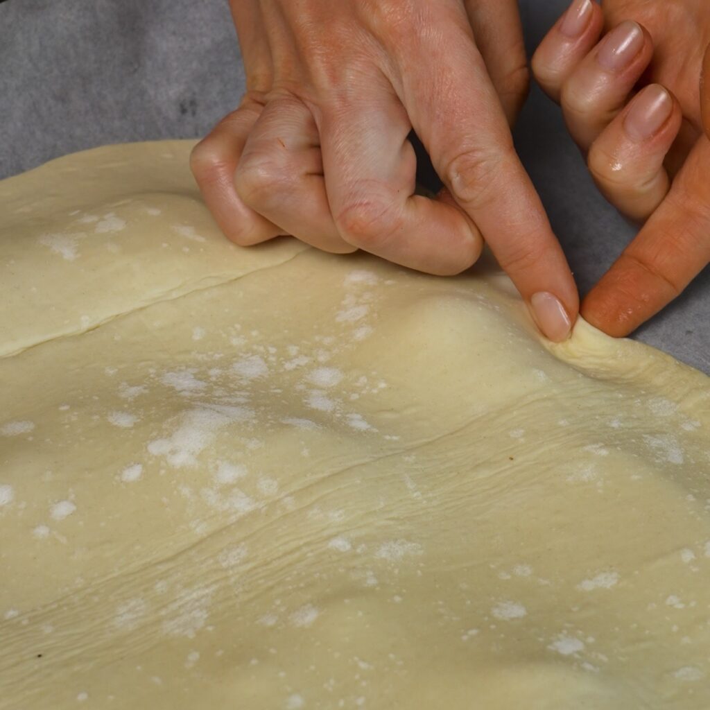 Hands crimp the edges of puff pastry over sliced tomatoes for an upside-down tomato tart.