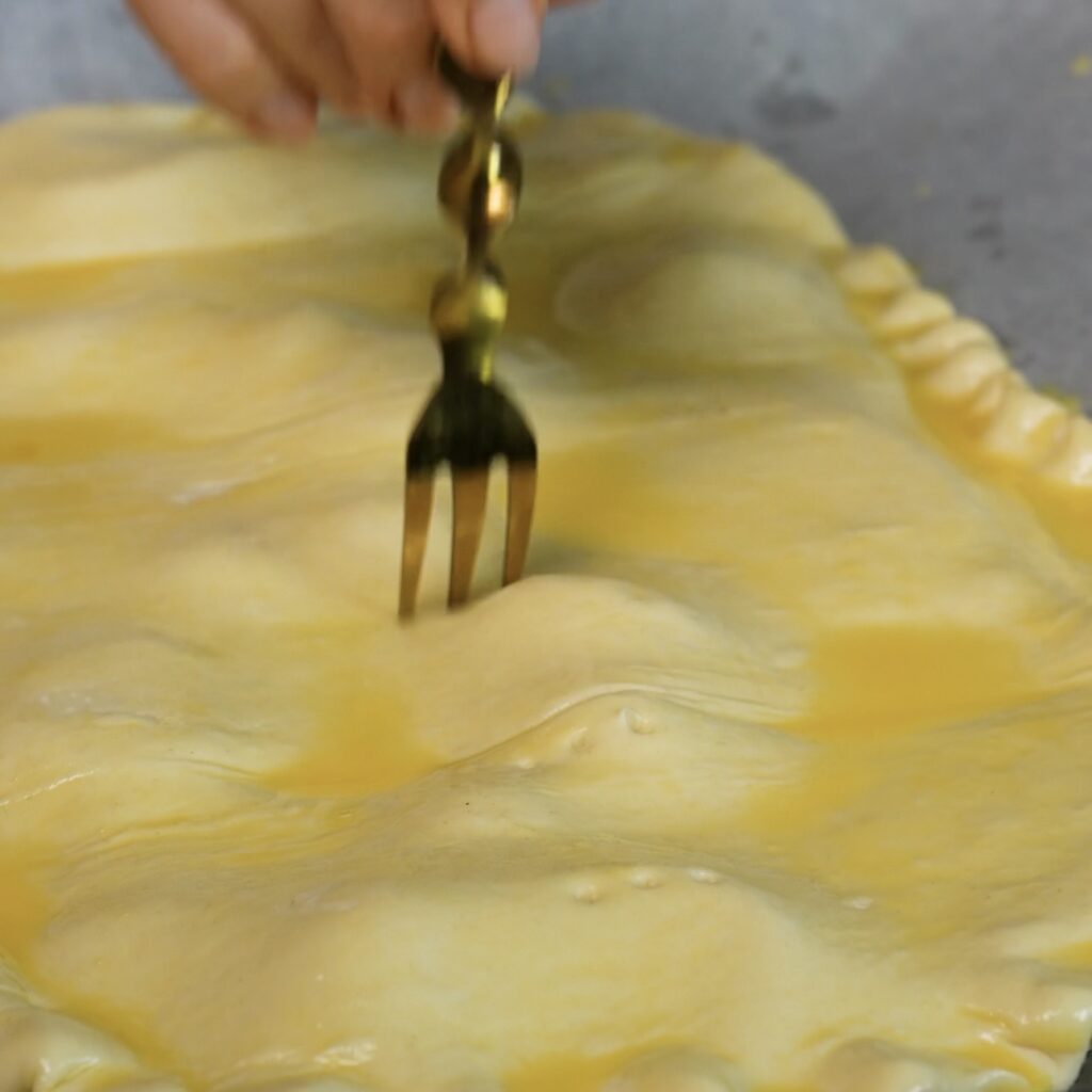 A fork pricks puff pastry before baking a tomato and stracciatella upside-down tart.