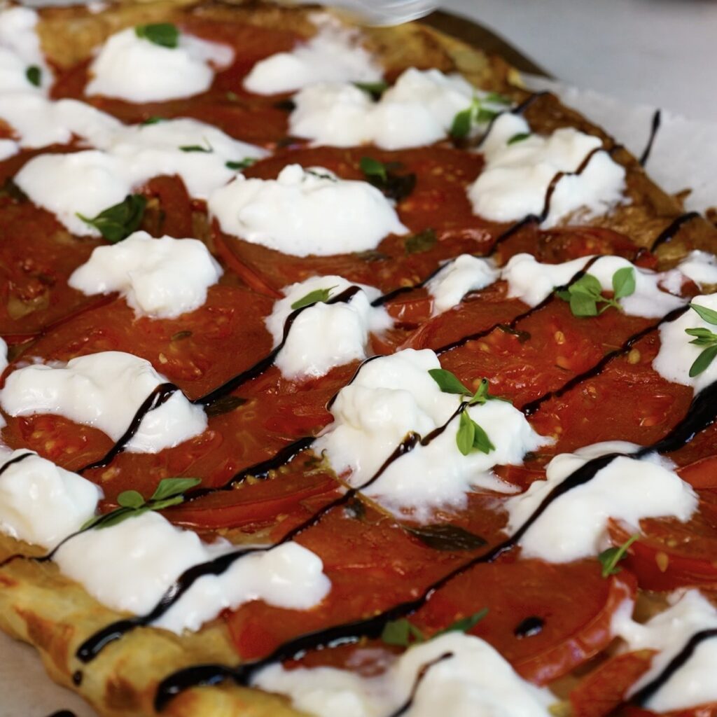 Tomato upside-down tart topped with stracciatella, balsamic glaze and fresh thyme leaves.