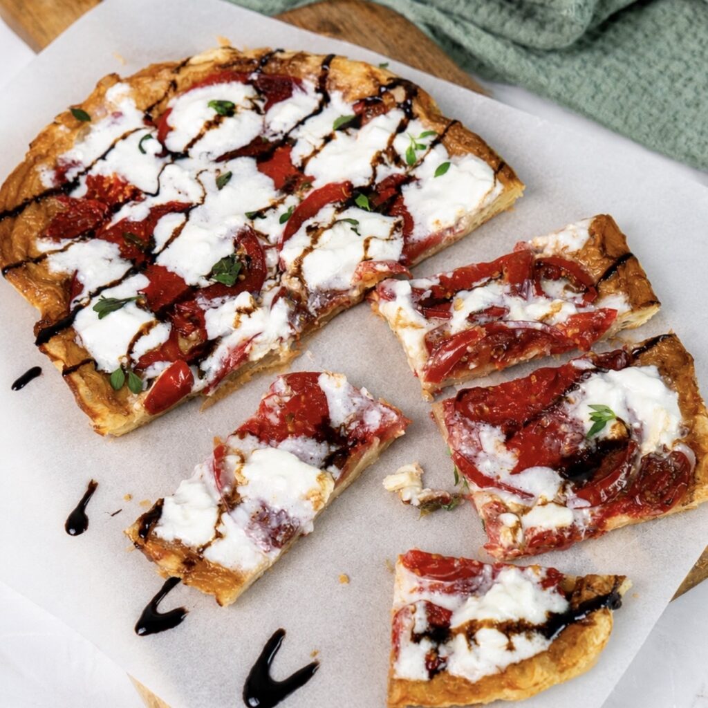 Sliced tomato and stracciatella upside-down tart served on a wooden board.