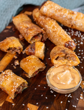 Rice paper cheeseburger rolls served on a wooden board with dipping sauce