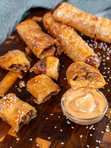 Rice paper cheeseburger rolls served on a wooden board with dipping sauce