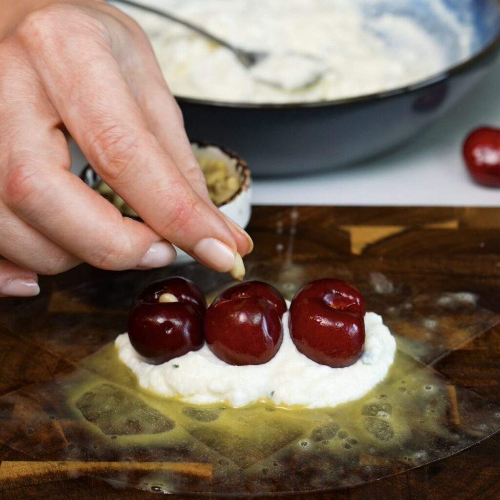 Stuffing pitted cherries with toasted pine nuts for cherry ricotta rice paper dumplings.