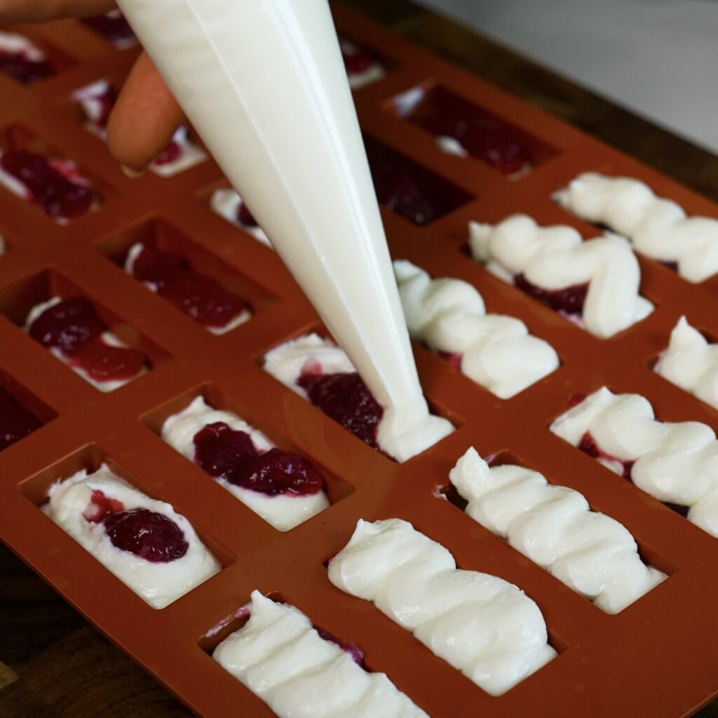 Silicone mould cavities filled with cottage cheese mixture and cherry sauce for frozen chocolate bars.