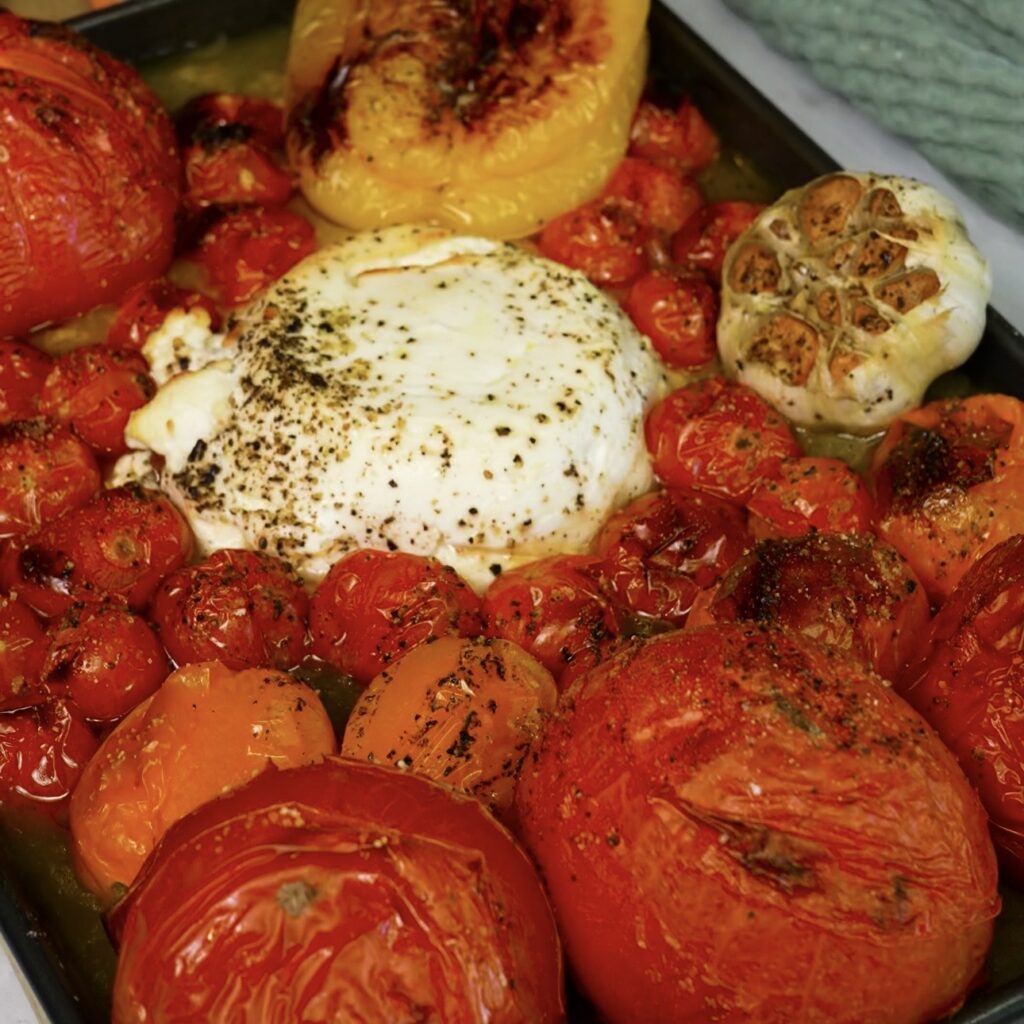 Roasted tomatoes, cherry tomatoes, bell pepper, garlic and ricotta on a baking tray.