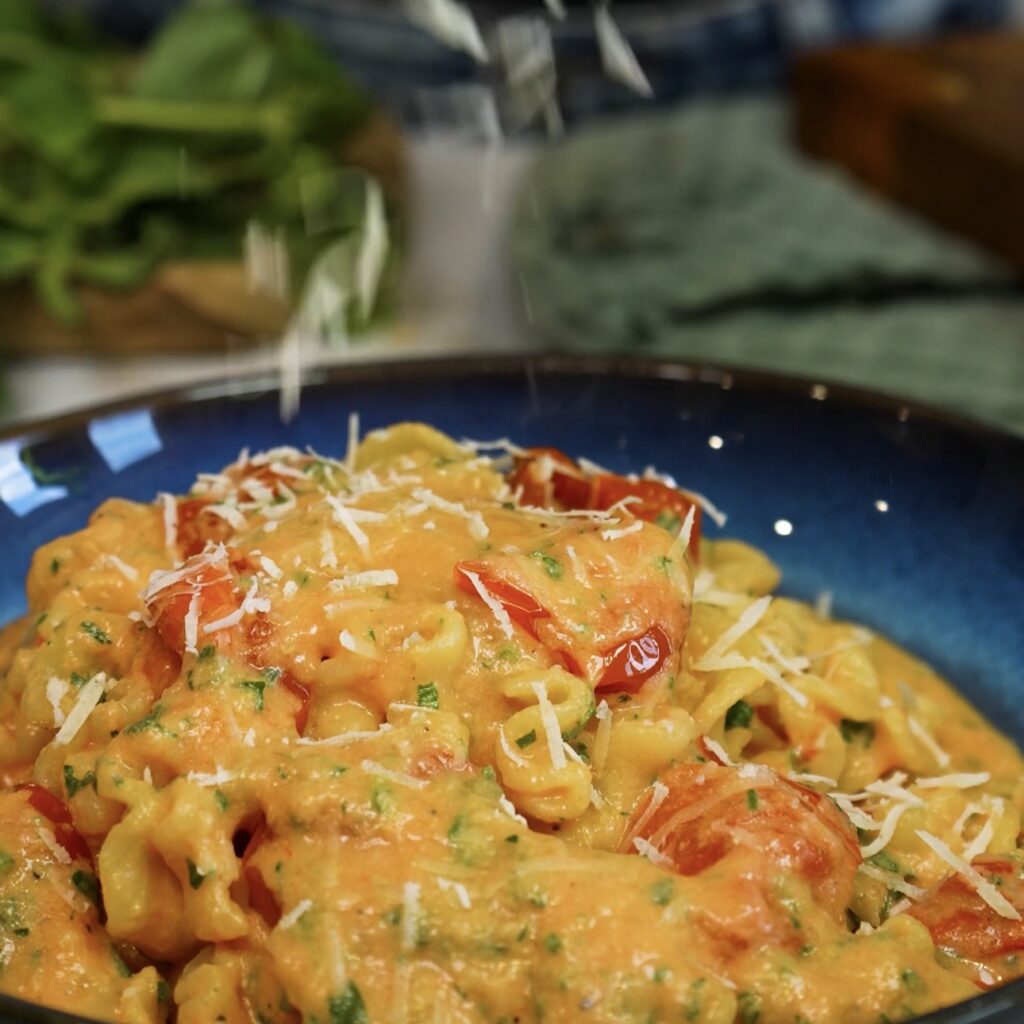 Roasted Tomato and Ricotta Pasta served on a plate while Parmesan is grated over the top.