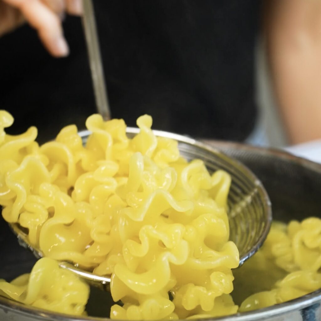 Cooked pasta being lifted from a pot with a slotted spoon before adding it to the sauce.