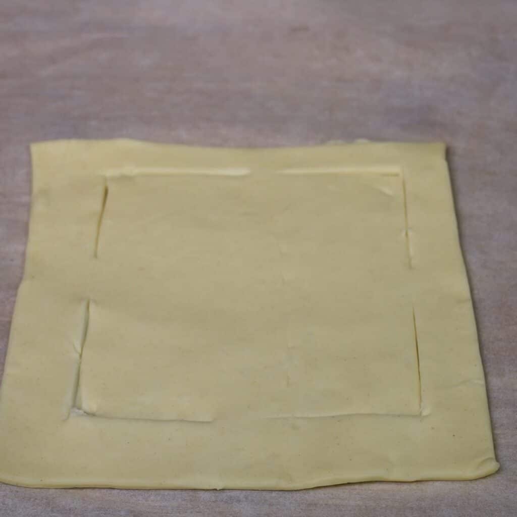 Four corners of a smaller inner square cut into a puff pastry square, leaving the middle of each side connected.