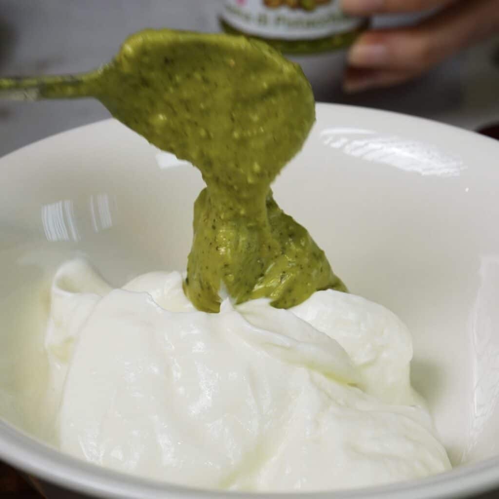 Thick plain yoghurt being mixed with pistachio cream in a bowl.