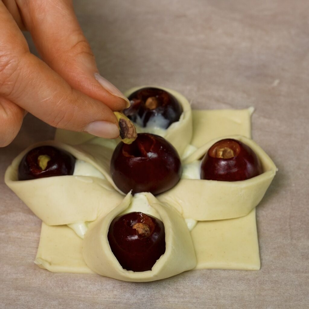 Pistachio kernels being inserted into the centres of pitted cherries on shaped puff pastry.