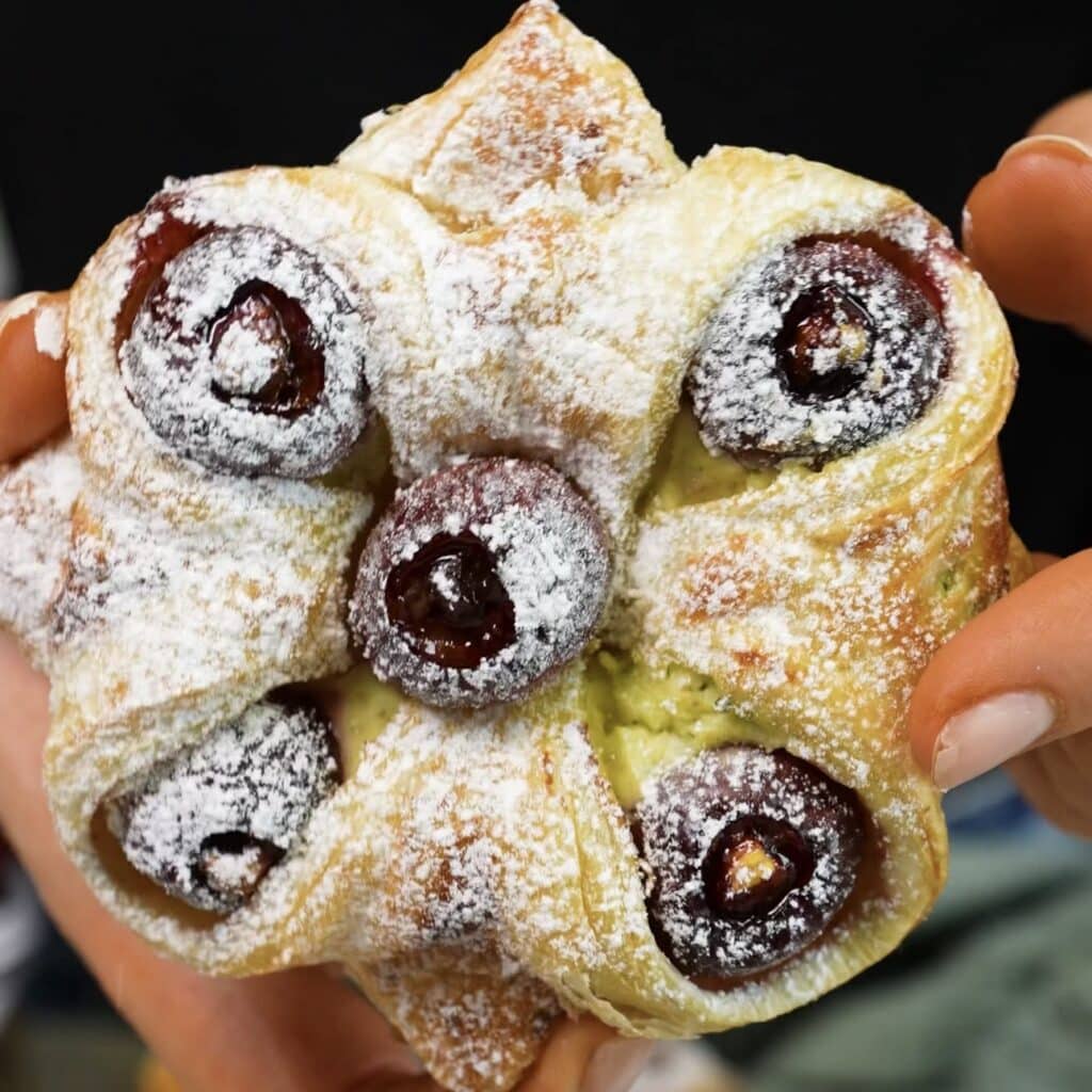 Hands holding a freshly baked Cherry and Pistachio Yogurt Puff.