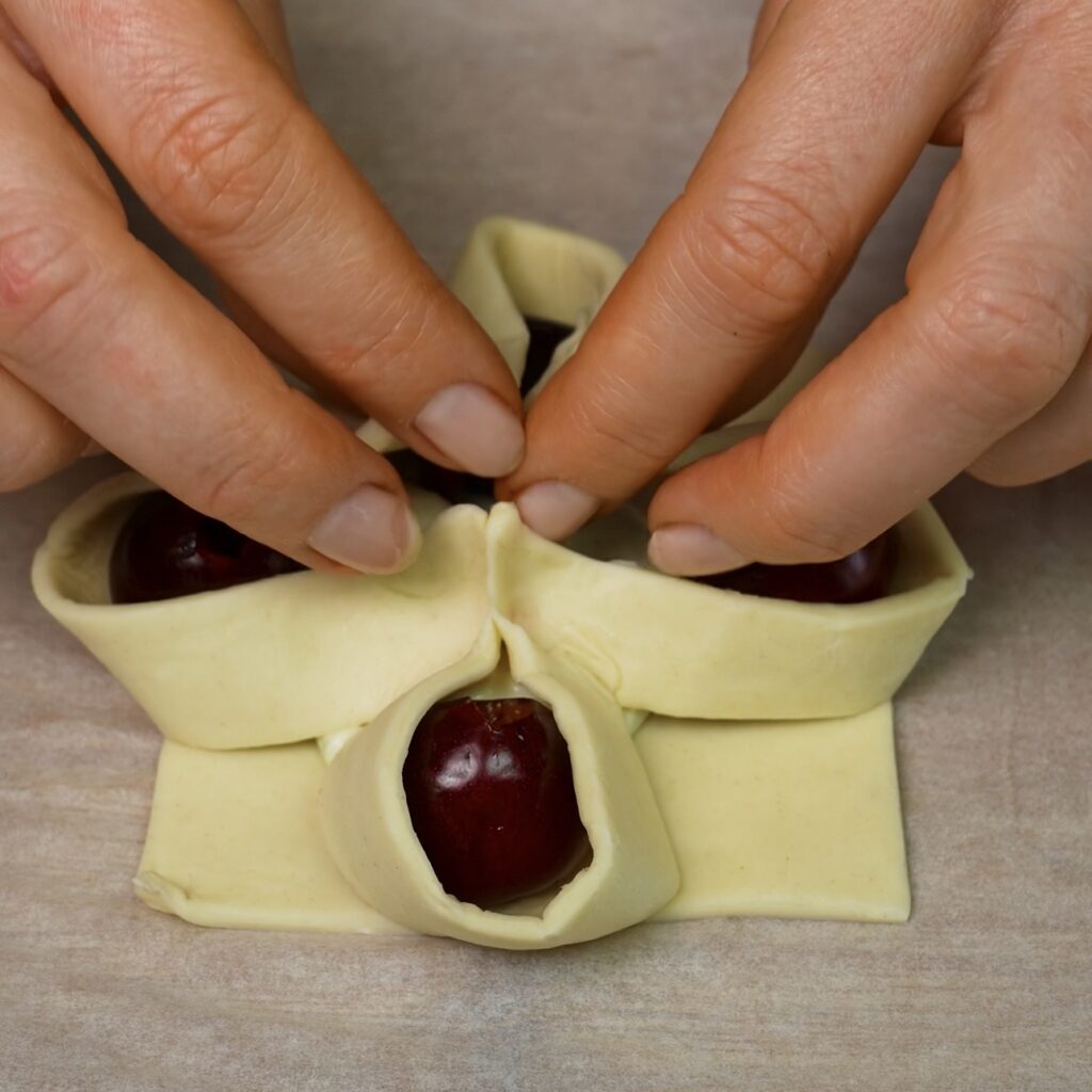 Four corners of a puff pastry square being brought together in the centre and secured.