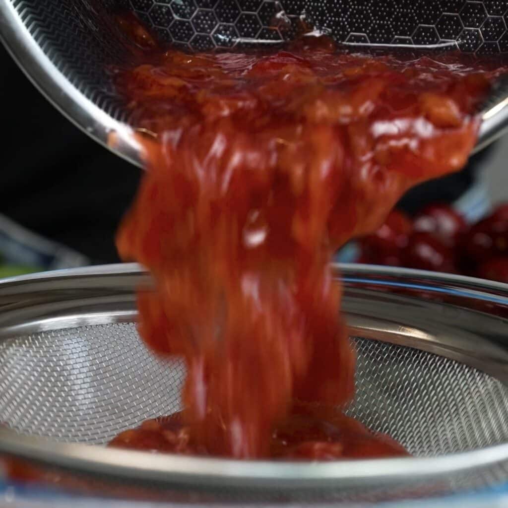 Passing homemade cherry sauce through a fine sieve