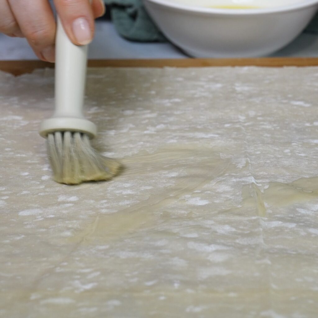 Brushing a filo pastry sheet with melted butter for Cheesy Beef Ragù Filo Rolls
