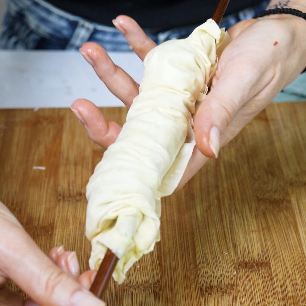 Removing the chopstick from the crinkled filo pastry roll