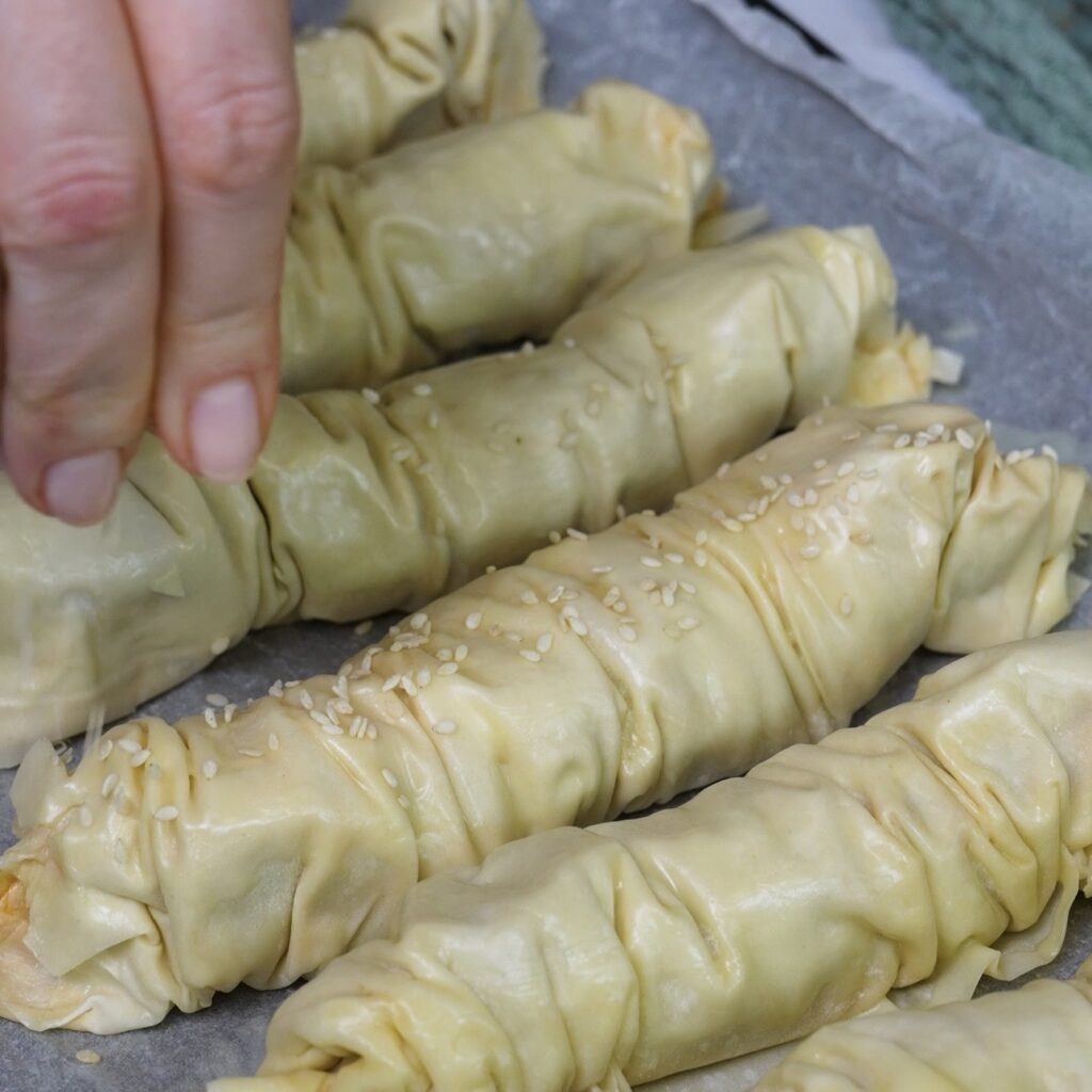 Sprinkling sesame seeds over the buttered crinkled filo rolls before baking