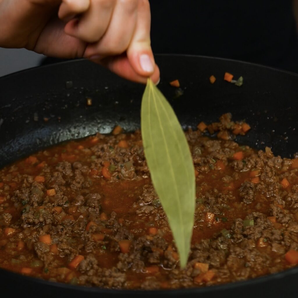 Adding a bay leaf to the beef ragù while it simmers