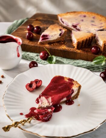 Slice of Cherry Cheesecake served on a plate with cherry sauce, with the remaining cheesecake in the background