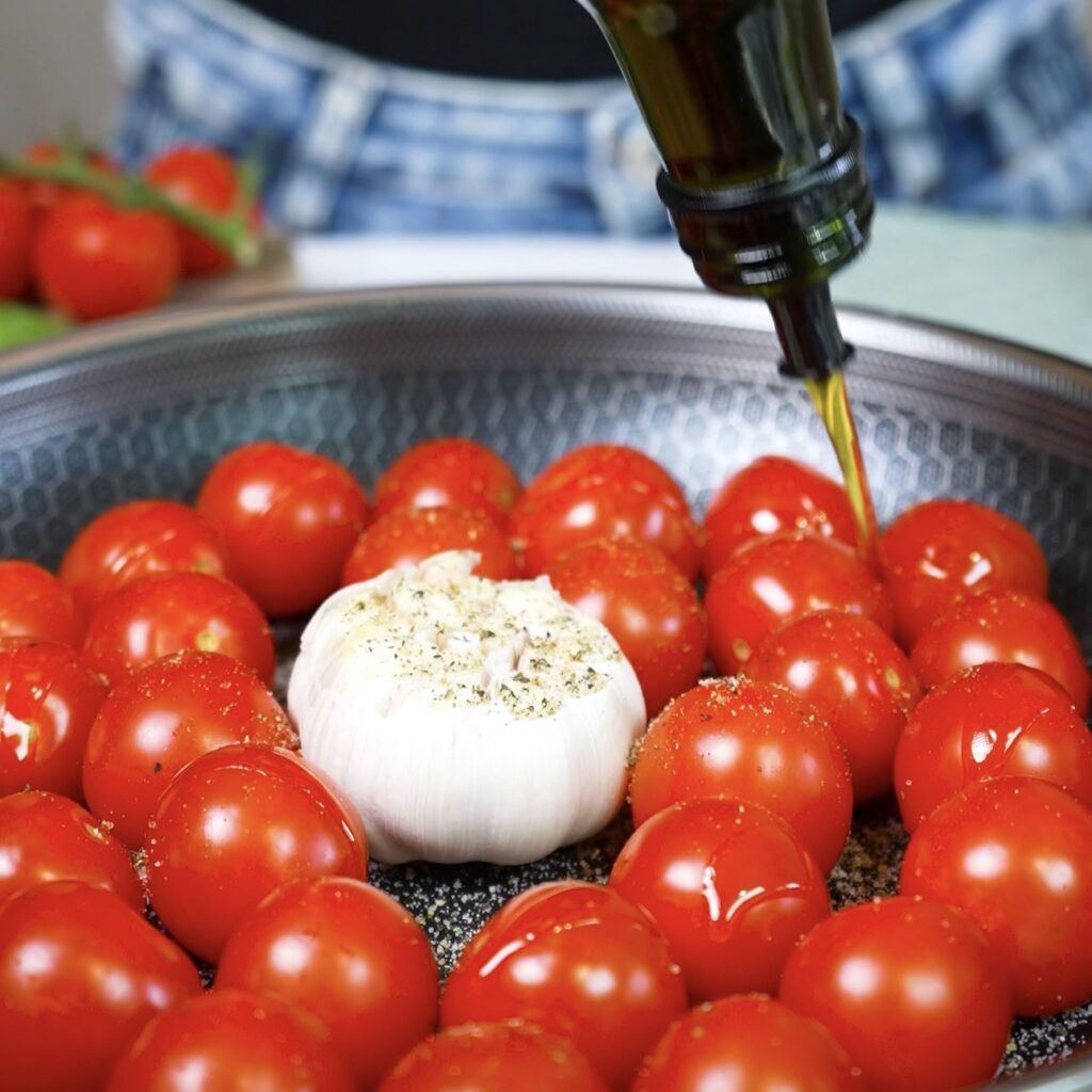 Cherry tomatoes and a garlic bulb seasoned in an ovenproof pan before roasting.