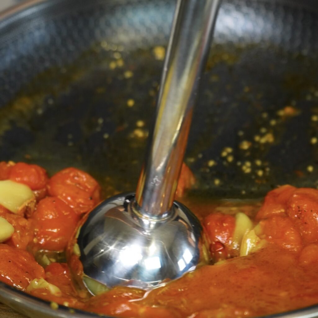 Blending the roasted tomato and garlic sauce with an immersion blender.