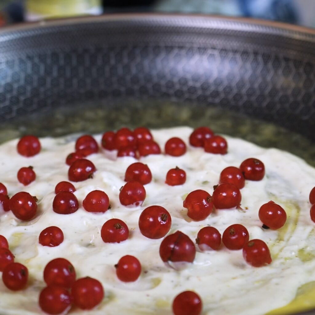Pistachio yoghurt filling and redcurrants added to the layered rice paper pancake in a frying pan.