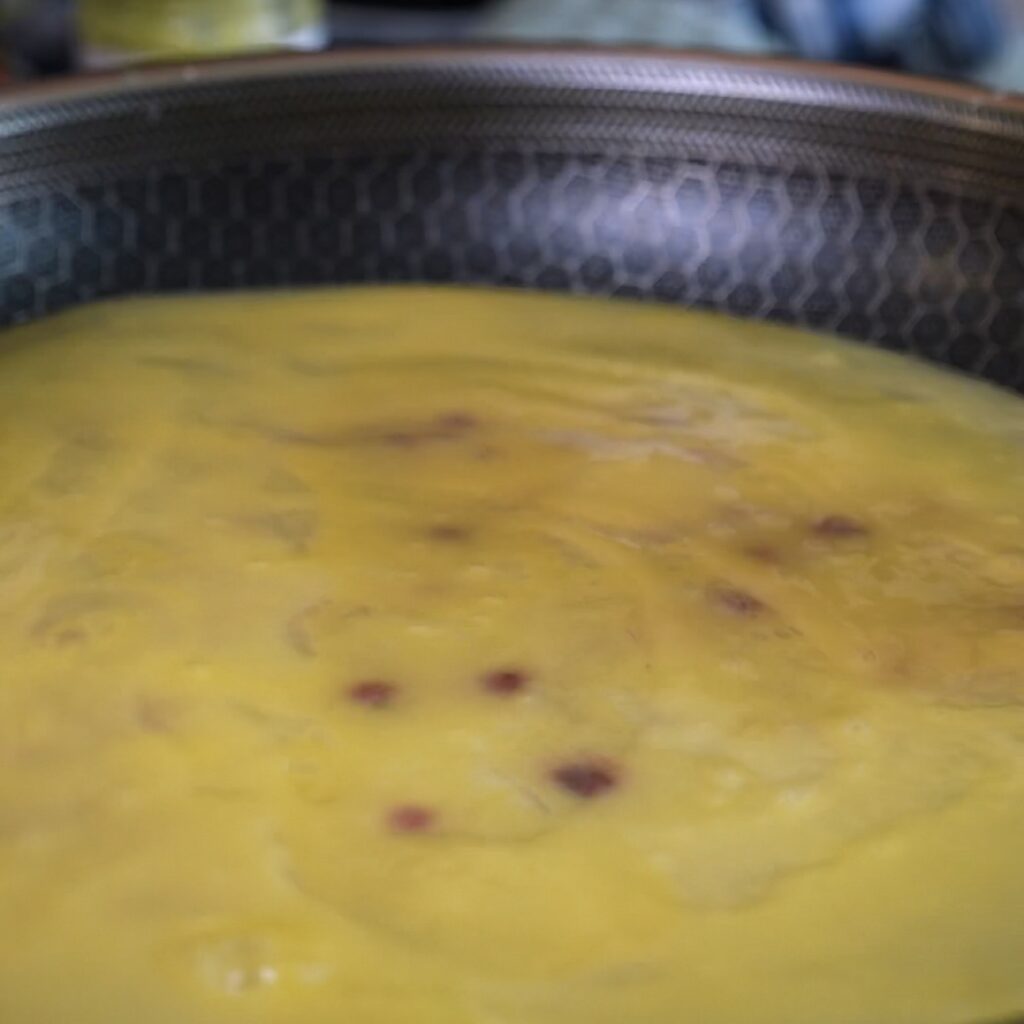Redcurrant and pistachio yoghurt filling covered with two egg-dipped rice paper sheets in a frying pan.