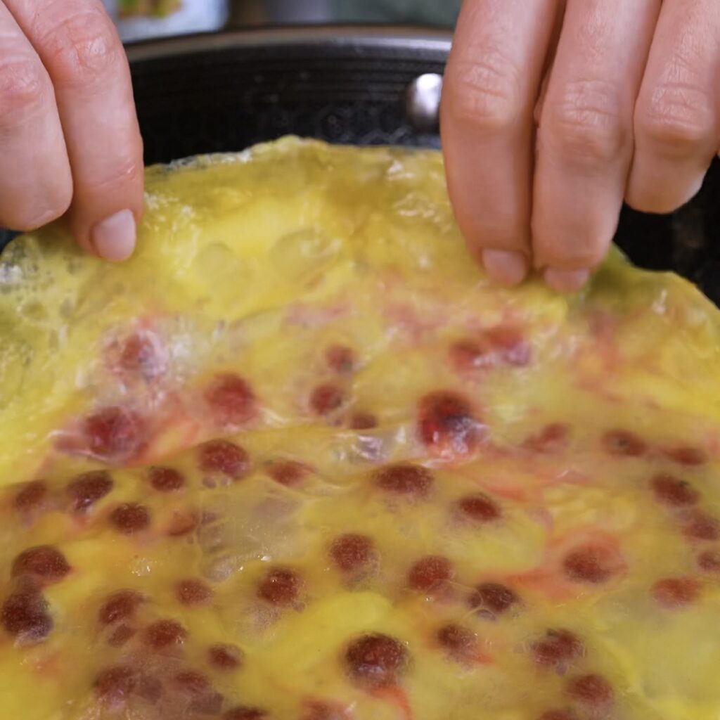Redcurrant rice paper pancake being flipped in a frying pan during cooking.