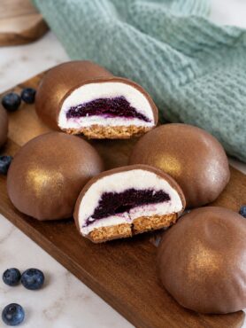 Blueberry Cottage Cheese Chocolate Spheres on a wooden board, with one sphere cut in half to reveal the creamy filling and blueberry centre.