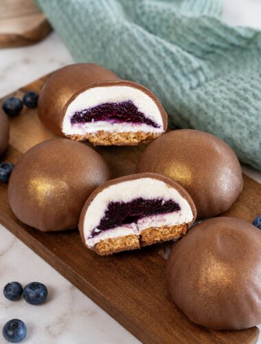 Blueberry Cottage Cheese Chocolate Spheres on a wooden board, with one sphere cut in half to reveal the creamy filling and blueberry centre.