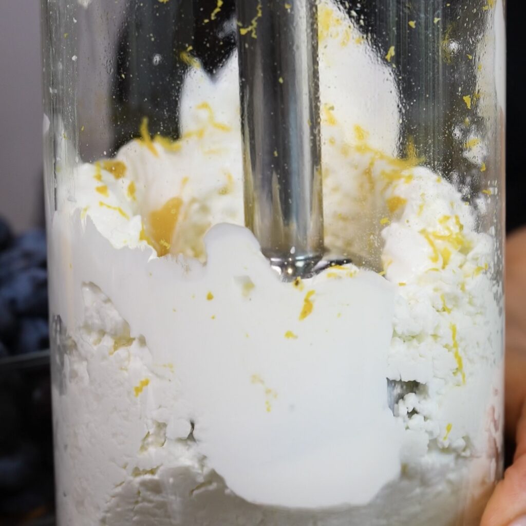 Cottage cheese mixture being blended with an immersion blender until smooth and creamy.