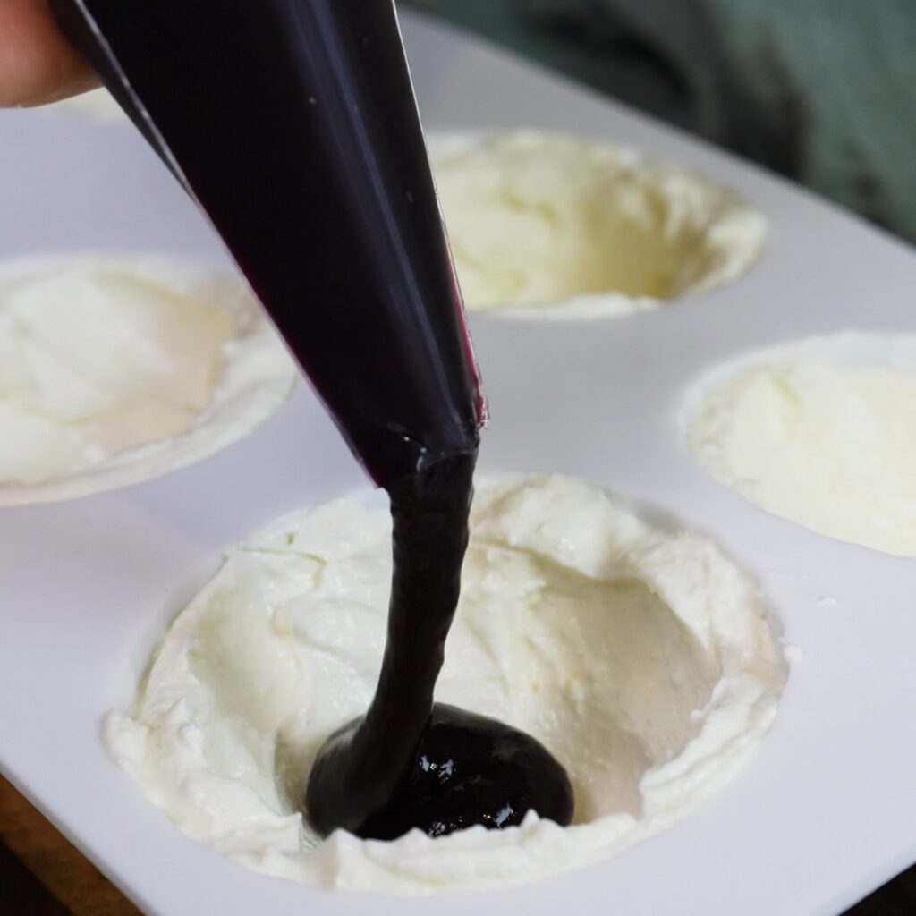 Blueberry sauce being added to the centre of the cottage cheese mixture in a silicone mould.