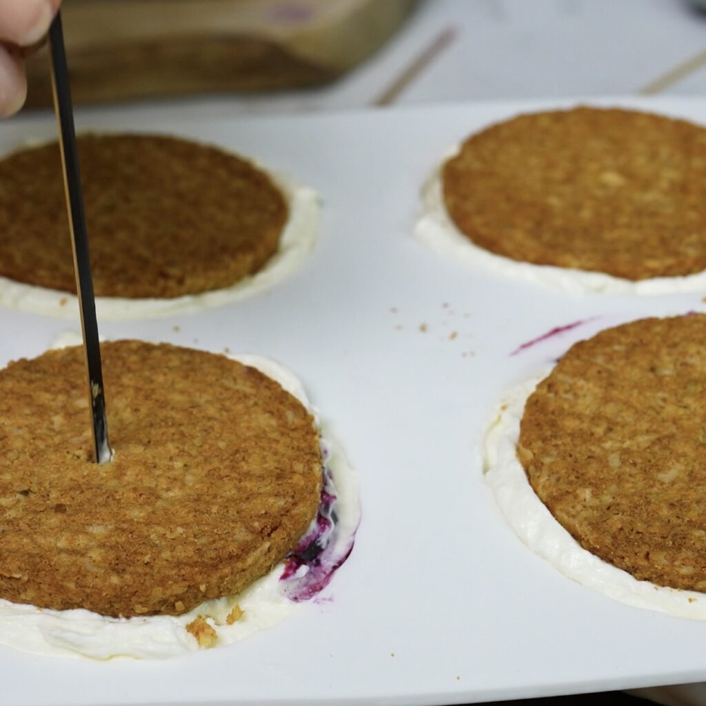 Toothpick being inserted through an oat cookie into a cottage cheese sphere in a silicone mould.