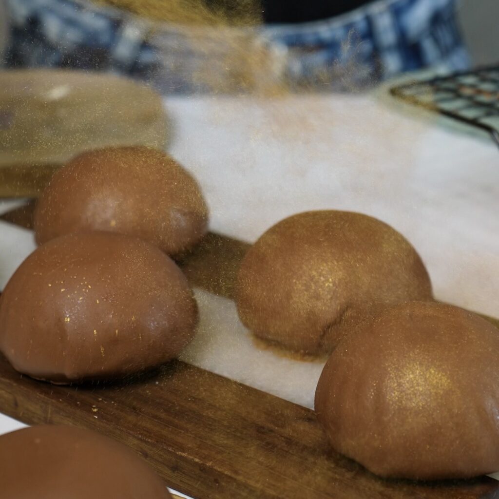Blueberry Cottage Cheese Chocolate Spheres being dusted with edible gold dust.