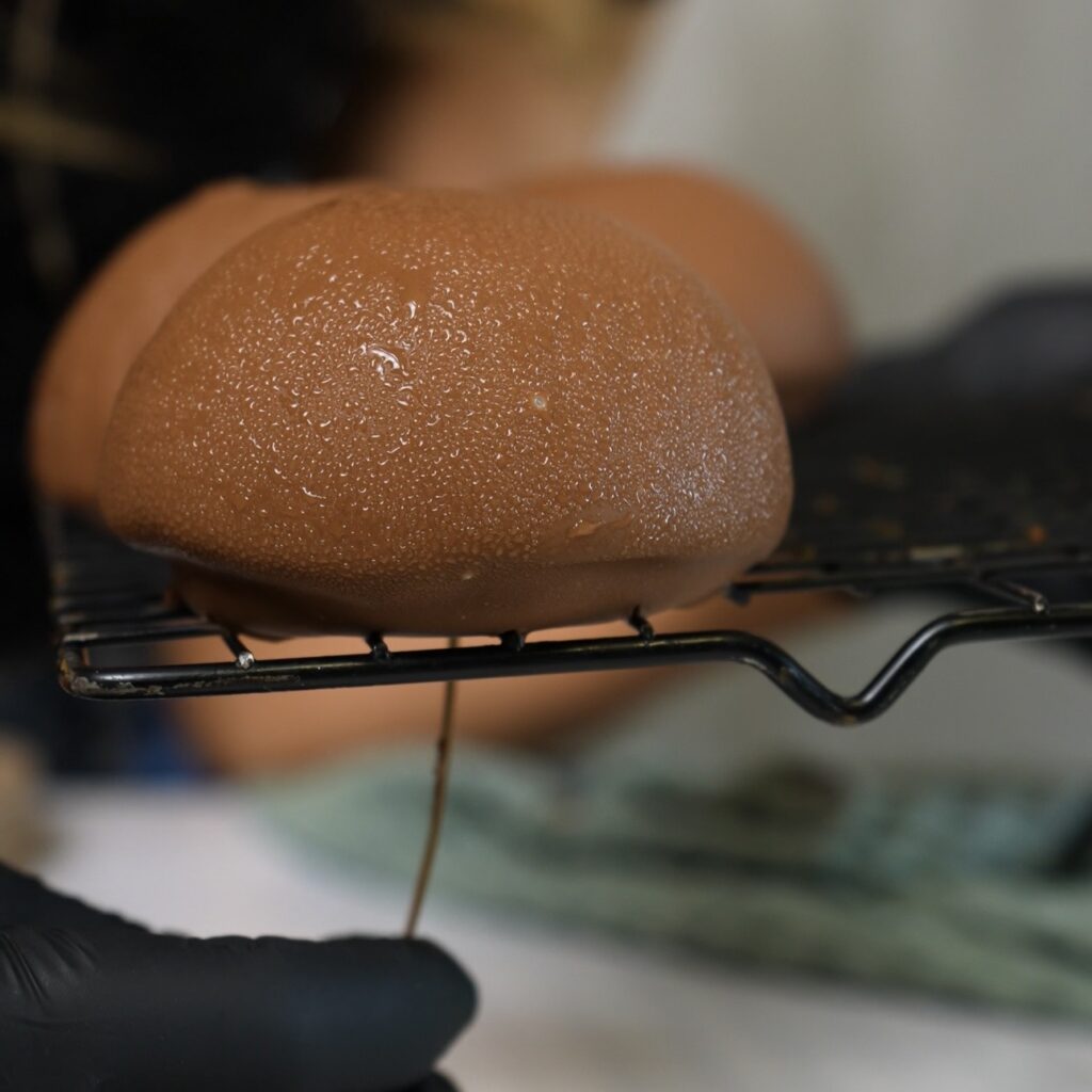 Toothpick being gently twisted and pulled out of a Blueberry Cottage Cheese Chocolate Sphere resting on a wire cooling rack.