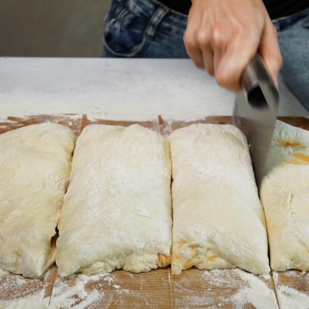 Filled bread dough being divided into equal portions with a dough scraper.
