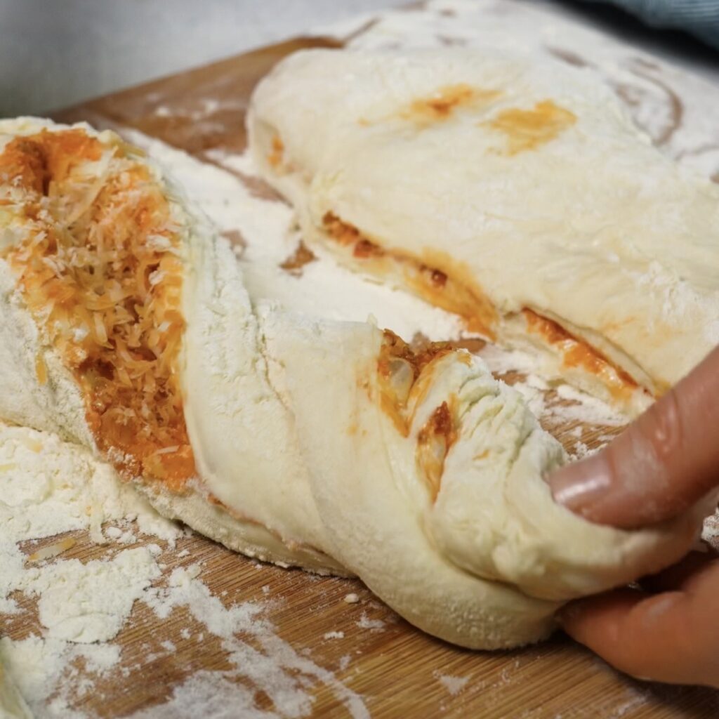 A portion of filled bread dough being gently twisted into a baguette shape.