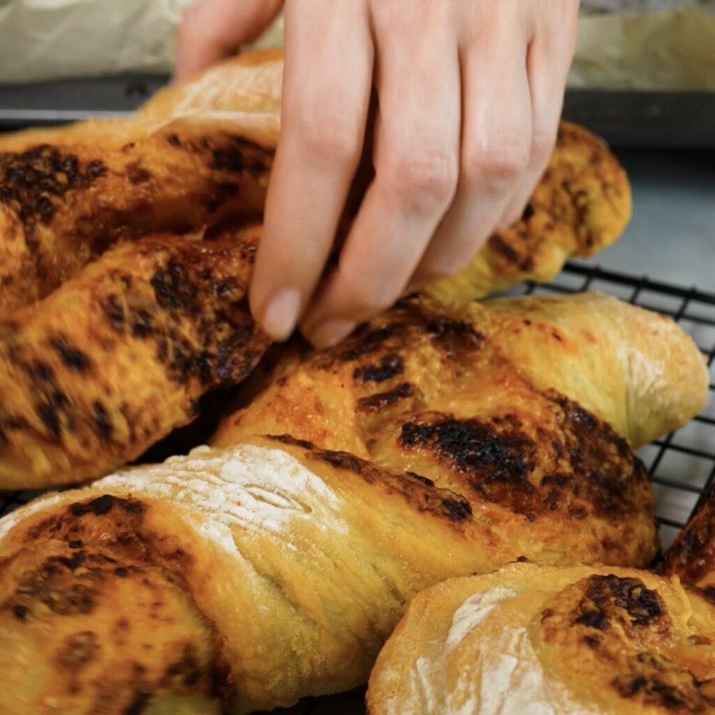 Freshly baked pesto and Parmesan twisted baguettes cooling on a wire rack.