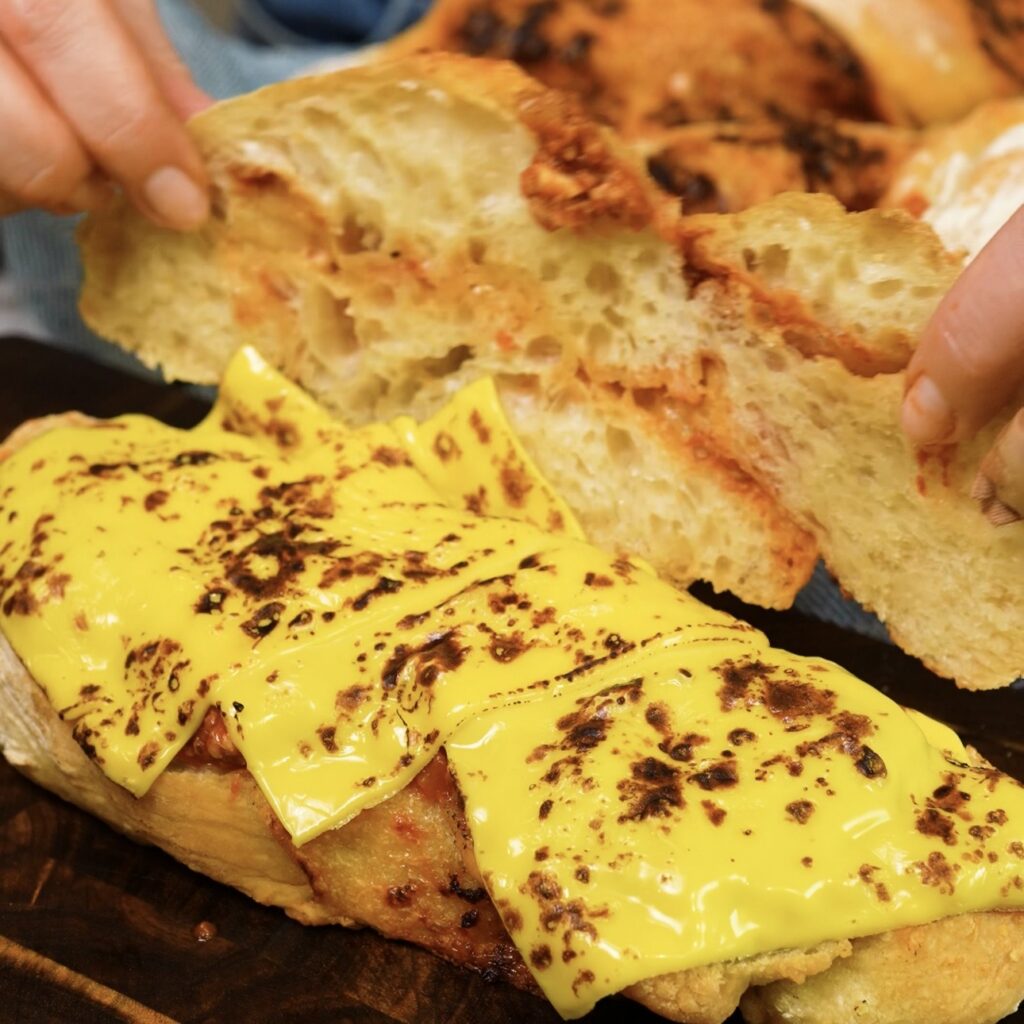 Pesto and Parmesan baguette being filled with beef ragù and cheese to make a warm sandwich.