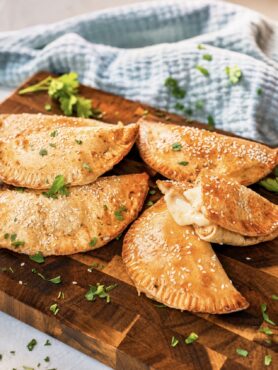 Cheesy Chicken Tortilla Pockets served on a wooden board, with one pocket broken apart to reveal the chicken and mozzarella filling.